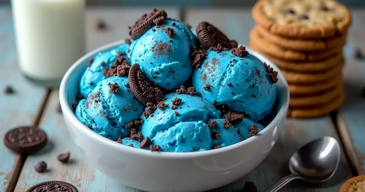 A creamy blue Cookie Monster ice cream served in a bowl, filled with crushed Oreo cookies and chocolate chips, with extra cookies on the side.